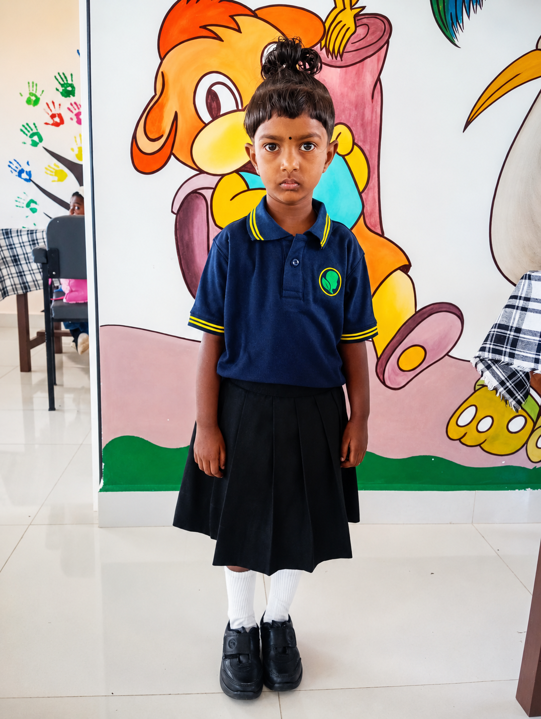 Tiny Seeds pre-school student in navy polo with yellow tipping, embroidered crest and pleated skirt