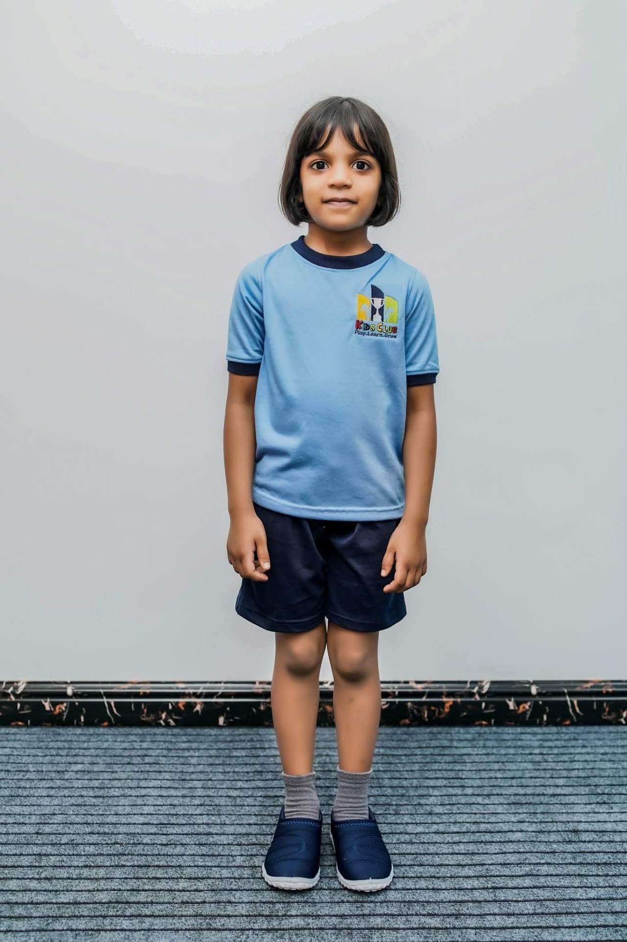 Kids Club Play Learn Grow pre-school student in sky blue Mezzo ringer tee with navy trim and navy shorts