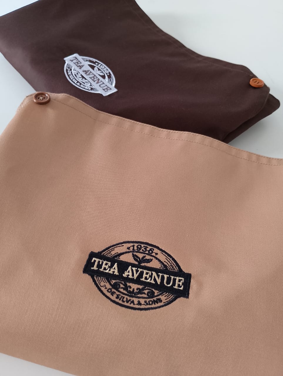 Tea Avenue De Silva & Sons brown and tan aprons with embroidered logo